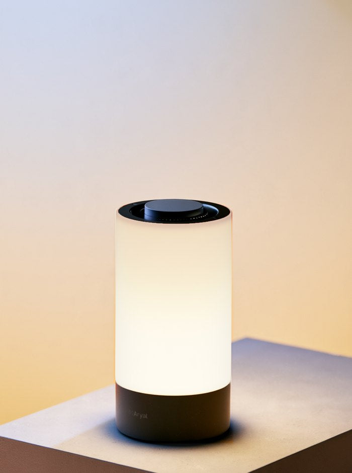 The Aryal lamp glowing bright white on a plinth, against a soft morning sky